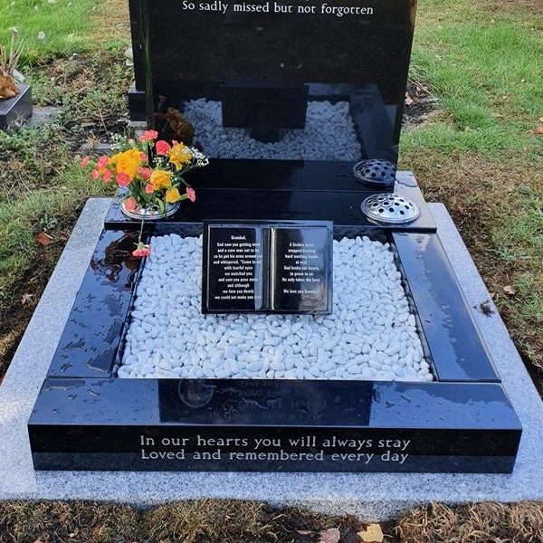 Black granite grave surround with book, inscription and white pebbles